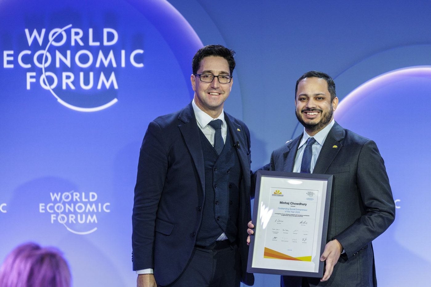 Minhaj Chowdhury receives the Schwab Foundation award certificate on the World Economic Forum stage, Davos 2026.